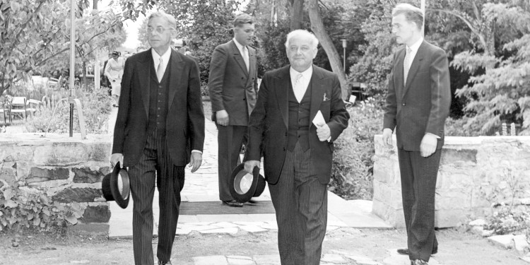 Die Schwarz-weiß-Aufnahme zeigt vier Männer in Anzügen im Botanischen Garten. Die beiden vorderen tragen einen Zylinder in der Hand und laufen in Richtung des Fotografen.<address>© Universitätsarchiv Münster</address>