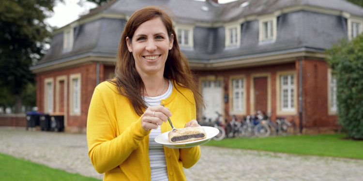Das Foto zeigt eine Frau, Stephanie Elias, die ein Stück Mohnkuchen in die Kamera hält.<address>&copy; Uni MS - Julia Harth</address>