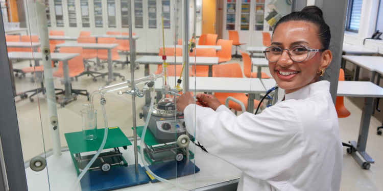 Das Bild zeigt Preyanka Chuntharakannan im Chemie-Seminarraum. Sie bereitet einen Versuch vor und trägt dabei Schutzbrille und weißen Kittel.<address>© Uni MS - Julia Harth</address>