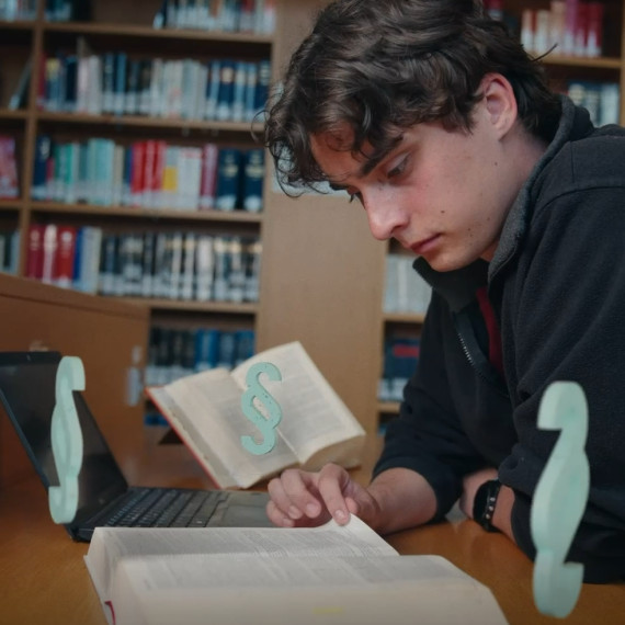 Das Foto zeigt einen Studenten. Er sitzt in einer Blbliothek und liest ein Buch. Vor ihm stehen animierte Paragraphen.<address>© Malte Papenfuss</address>