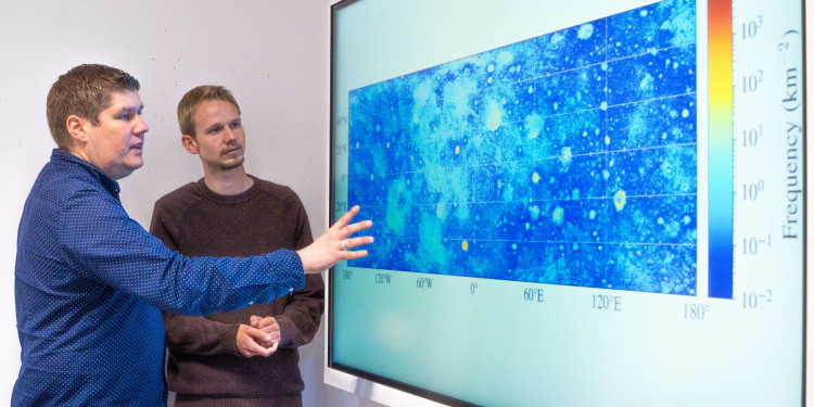 Prof. Dr. Bastian Gundlach und Doktorand Ben Aussel (v. l.) betrachten eine Karte der Mondoberfläche, die rund 94 Millionen Felsblöcke zeigt.<address>© Uni MS - Linus Peikenkamp</address>