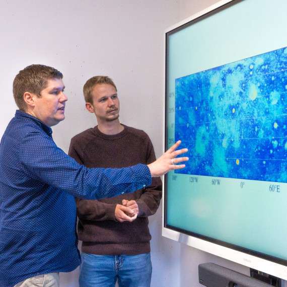 Prof. Bastian Gundlach and doctoral student Ben Aussel (from left) look at the map of the moon’s surface which shows around 94 million boulders.<address>© Uni MS - Linus Peikenkamp</address>