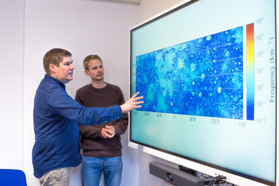 Prof. Bastian Gundlach and doctoral student Ben Aussel (from left) look at the map of the moon’s surface which shows around 94 million boulders.<address>&copy; Uni MS - Linus Peikenkamp</address>