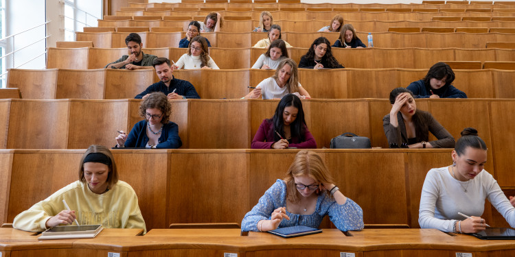 Studierende sitzen in einem Hörsaal mit hölzernen aufsteigenden Bänken.<address>© Uni MS - Johannes Wulf</address>