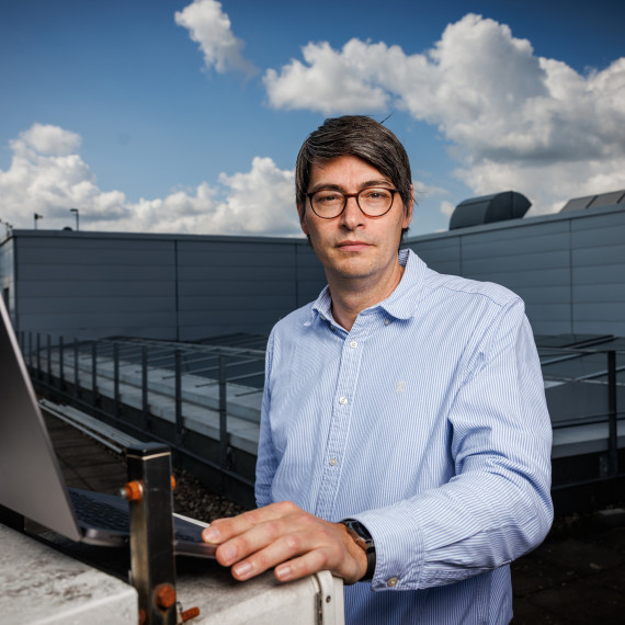 Benjamin Risse looks into the camera. He is standing on the roof of the GEO-I building, with a laptop in front of him.<address>© Uni MS - Peter Leßmann</address>