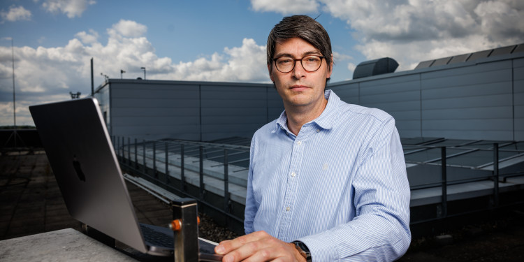 Benjamin Risse looks into the camera. He is standing on the roof of the GEO-I building, with a laptop in front of him.<address>© Uni MS - Peter Leßmann</address>