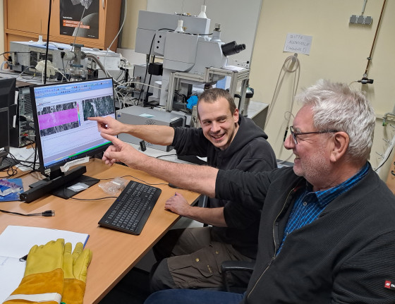 Prof. Dr. Bischoff and Dr. Maximilian P. Reitze can be seen working on an infrared spectrometer with a microscope and looking at a screen.<address>© M.P. Reitze</address>