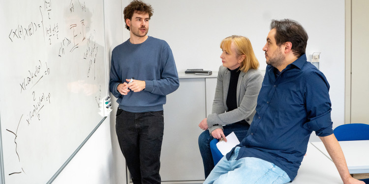 Dr. Johannes Pirsch, Prof. Dr. Anna Kulesza und Dr. Domenico Bonocore (v. l.) vor einem mit Formeln beschrifteten Whiteboard in einem Seminarraum<address>© Uni MS - Linus Peikenkamp</address>