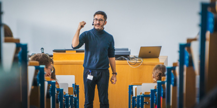 Ein Mann, Dr. Dogus Darici, hält im Hörsaal eine Vorlesung. Er steht vor den Sitzreihen am Pult und spricht gestikulierend zu den Studierenden.<address>© Uni MS - Linus Peikenkamp</address>