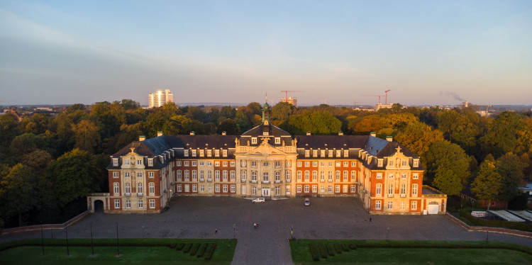 Zu sehen ist ein Drohnenfoto vom Schloss im Abendlicht.<address>&copy; Uni MS - Johannes Wulf</address>