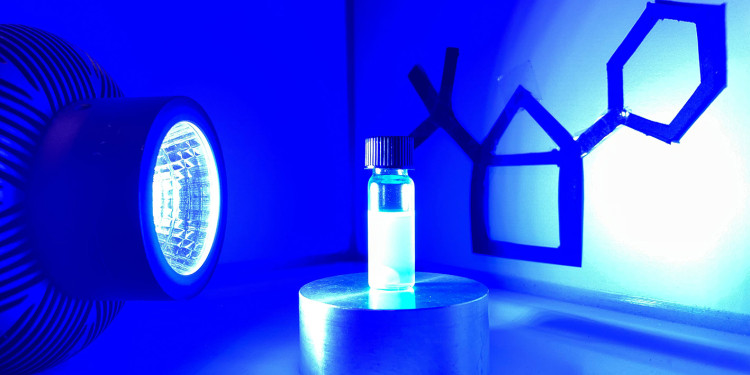 The chemists used this experimental setup to synthesize Hausan. The blue light from the lamp (left in the image) activates the photocatalyst (center, in the reaction vessel), which enables the reaction. On the right side of the image, the structure of a Hausan with two side chains can be seen symbolically.<address>&copy; Glorius Group</address>