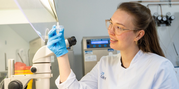 A scientist holds a sample dish and examines it under a microscope in a medical laboratory.<address>&copy; Uni MS - Linus Peikenkamp</address>