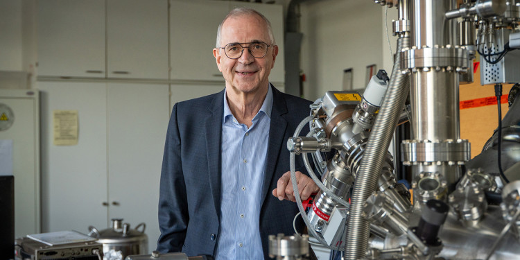 Prof. Dr. Harald Fuchs steht hinter einem - zum Teil sichtbaren - Rastersondenmikroskop in einem Labor und blickt in die Kamera (Porträtaufnahme).<address>&copy; Uni MS - Linus Peikenkamp</address>