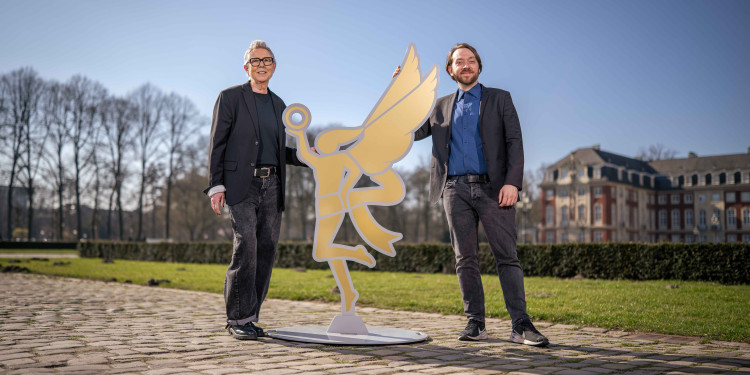 Das Bild zeigt Barbara Wicher links und Tim Zemicka rechts neben der lebensgroßen goldenen Nike-Figur. Beide stehen im Sonnenschein draußen mit dem Schloss weit im Hintergrund.<address>&copy; Thomas Mohn</address>