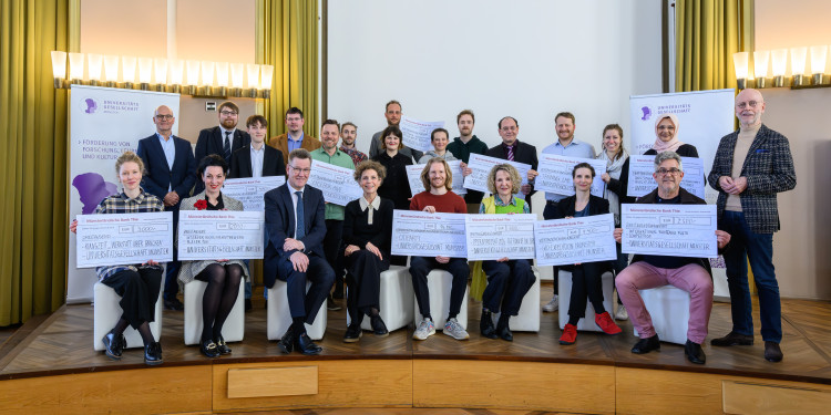 Auf dem Bild sind zahlreiche Personen zu sehen. Viele von ihnen halten große symbolische Schecks in der Hand und schauen in die Kamera.<address>&copy; Universitätsgesellschaft Münster - Michael Möller</address>