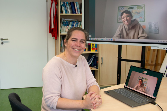 The photo shows Prof. Dr Angela Schwering at her desk and Master’s graduate Selani Thomas on a large screen next to her (joining via video link from Lisbon).<address>&copy; University of Münster - Brigitte Heeke</address>