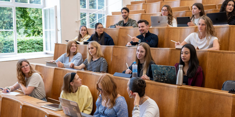 Das Bild zeigt einen Vorlesungssaal mit Holzbänken in denen junge Frauen und Männer sitzen.<address>&copy; Uni MS - Johannes Wulf</address>