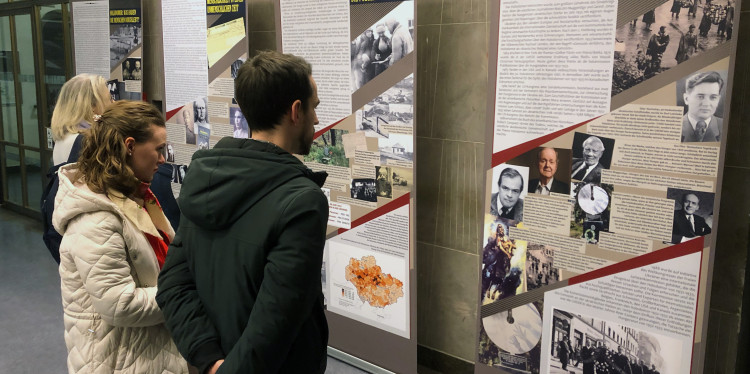 Drei Menschen stehen im Gebäue der Ludwig-Maximilians-Universität München vor den Stellwänden der Ausstellung „Wieso seid ihr noch am Leben?“.<address>&copy; LMU München - Gerhard Gnauck</address>