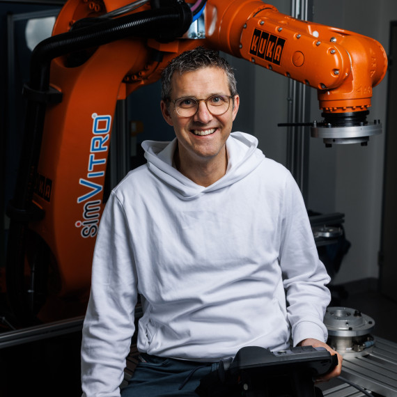 Das Bild zeigt Mirco Herbort an einem medizinischen Roboter. Er trägt einen weißen Pullover und lacht in die Kamera.<address>&copy; Uni MS - Peter Leßmann</address>