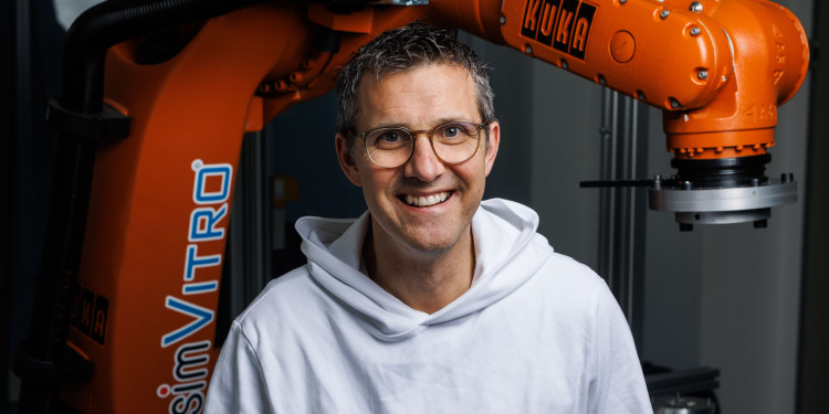 Das Bild zeigt Mirco Herbort an einem medizinischen Roboter. Er trägt einen weißen Pullover und lacht in die Kamera.<address>&copy; Uni MS - Peter Leßmann</address>
