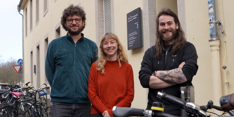 Anton Schütt (links), Anne Degen und Janis Liebetruth stehen nebeneinander zwischen den Fahrradständern vor dem Haus an der Wilmergasse 2 und schauen in die Kamera.<address>&copy; Uni MS - Julia Harth</address>
