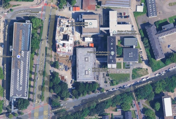 Satellitenaufnahme von Google Maps. Zu sehen ist das Areal am Coesfelder Kreuz in Münster aus der Vogelperspektive mit den bestehenden Gebäuden der Mathematik und Informatik, umliegenden Grünflächen und Straßen.<address>&copy; Google Maps</address>