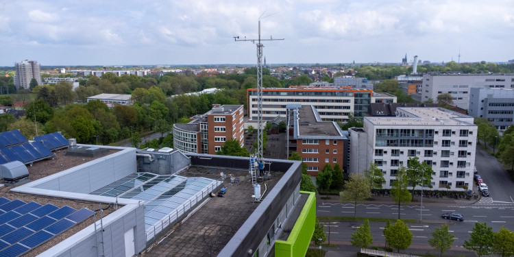 Aerial view of the GEO1 building, with the measurement tower rising several metres above one side of it. The skyline of the city of Münster can be seen in the background.<address>&copy; Uni MS - Johannes Wulf</address>