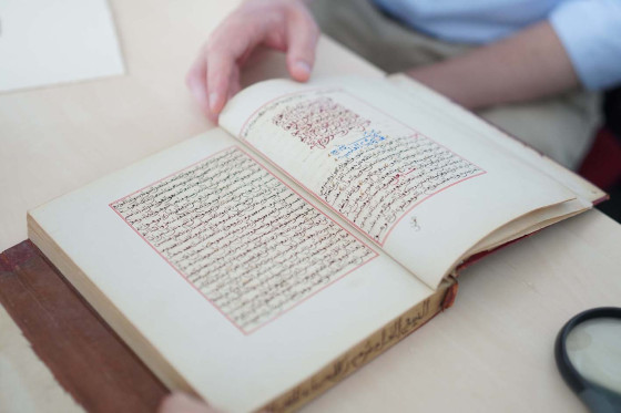 Handschrift (Buch) mit arabischen Schriftzeichen. Das Buch ist aufgeblättert, eine Hand hält die Seiten fest.<address>&copy; Uni MS - Julia Harth</address>