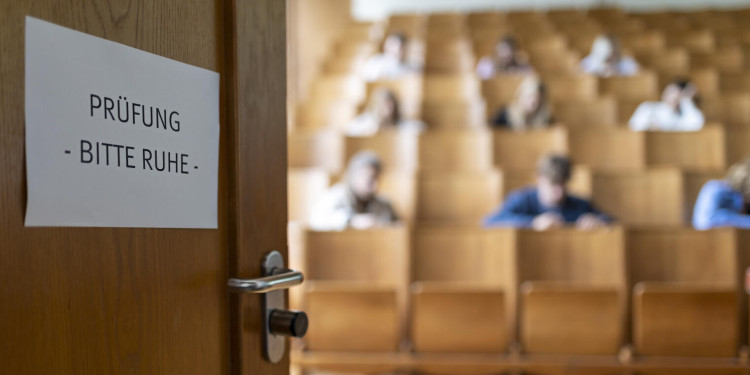 Studierende sitzen in einem Hörsaal und schreiben eine Prüfung. An der Tür klebt ein Zettel auf dem "Prüfung - bitte Ruhe" steht.<address>&copy; Uni MS - Nike Gais</address>