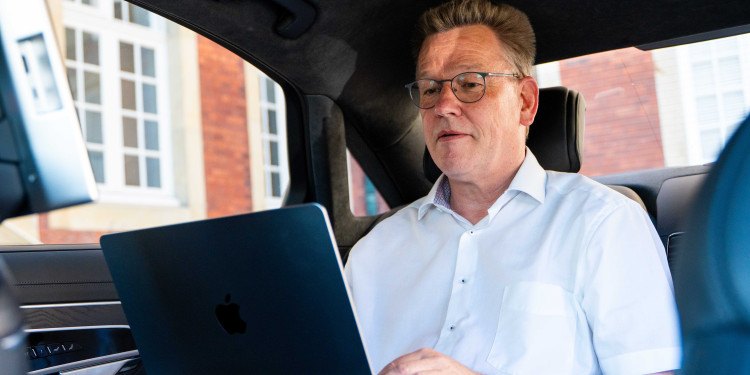 Das Bild zeigt den Rektor beim Arbeiten am Laptop in seinem Dienstwagen.<address>&copy; Uni MS - Linus Peikenkamp</address>