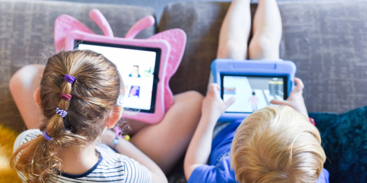 Das Bild zeigt zwei jüngere Kinder von oben fotografiert, die auf einem Sofa sitzen und auf Tablets schauen.<address>&copy; stock.adobe.com - tommoh29</address>