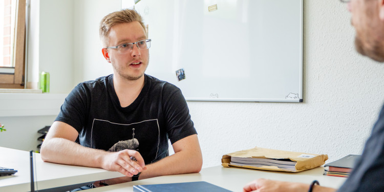 Auf dem Bild ist Luca Winkler in seinem Büro zu sehen. Er ist einem Gesprächspartner zugewandt.<address>&copy; Uni MS – Linus Peikenkamp</address>