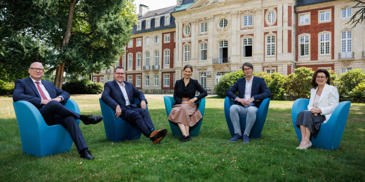 The photo shows the five new University Management members sitting next to each other in blue chairs in the green area behind the Schloss.<address>&copy; University of Münster - Peter Leßmann</address>