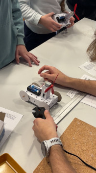 Auf dem Foto sind Kinderhände zu sehen, die ein batteriebetriebenes Mini-Pappfahrzeug bauen.<address>&copy; Q.UNI/ Daniela Klümper</address>