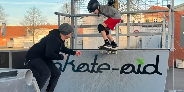 Der Skateboard-Pionier Titus Dittmann gibt einem Kind Hilfestellung, das mit einem Skateboard eine Miniramp herunterfährt.<address>&copy; Kai Reinhart</address>
