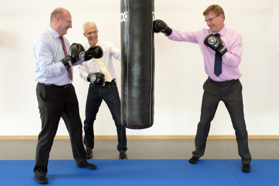 Three men are surrounding a punching bag, pretending to hit it.<address>&copy; Uni MS - Peter Grewer</address>