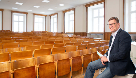 Rector Johannes Wessels is sitting at the lectern inside an empty lecture hall.<address>&copy; Uni MS - Peter Leßmann</address>