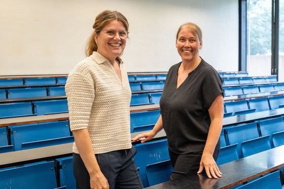 Zwei Frauen stehen in einem Hörsaal mit blauen Bänken<address>&copy; Uni MS - K. Kottke</address>