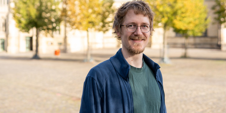 Ein Mann (Brustporträt) steht im Freien auf einem weiten, gepflasterten Platz. Der Hintergrund ist unscharf; man erkennt einige Bäume und den Teil einer Kirche/eines Doms.<address>&copy; Uni MS - Johannes Wulf</address>