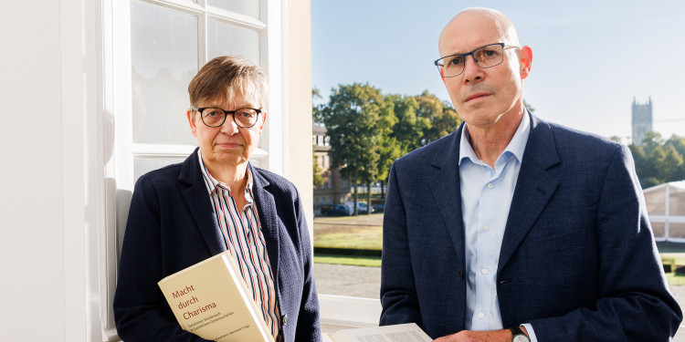 Das Bild zeigt Judith Könemann und Bernhard Frings. Sie stehen vor einem offenen Fenster. In den Händen halten die beiden jeweils ein Exemplar ihres Buchs „Macht durch Charisma. Geistlicher Missbrauch in Geistlichen Gemeinschaften“.<address>&copy; Uni MS - Peter Leßmann</address>