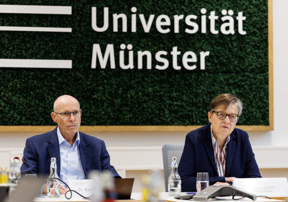 Das Bild zeigt Judith Könemann und Bernhard Frings. Sie sitzen an einem Tisch und sprechen zu Journalisten. Im Hintergrund ist der Schriftzug „Universität Münster“ zu sehen.<address>&copy; Uni MS - Peter Leßmann</address>