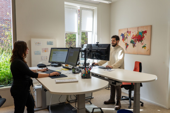 Das Foto zeigt ein Büro mit zwei Arbeitsplätzen. Hinter den Schreibtischen stehen eine Mitarbeiterin und ein Mitarbeiter des Studierendensekretariats.<address>&copy; Uni MS - André Bednarz</address>