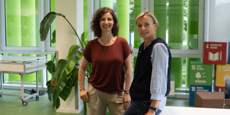 Dr. Nadine Rosendahl (links) und Dr. Katja Wrenger stehen in einem Seminarraum und schauen in die Kamera. Die große Fensterfront im Hintergrund ist mit grünen Lamellen abgedunkelt.<address>&copy; Uni MS - Brigitte Heeke</address>