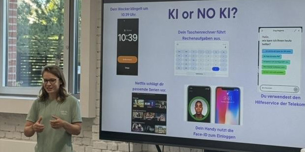 Eine Person steht in einer Unterrichtssituation/Präsentation vor einem Monitor. Darauf ist eine Folie mit der Überschrift "KI or NO KI?" zu sehen.<address>&copy; ifgi</address>