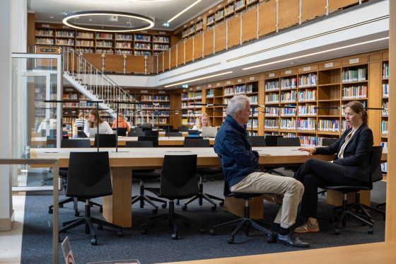 Rector Susanne Menzel-Riedl and press spokesperson Norbert Robers are sitting at a table in the law library and talking.<address>&copy; University of Münster - Johannes Wulf</address>