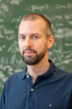 Zu sehen ist ein Porträt von Prof. Dr. Thomas Nikolaus vor einer grünen Tafel, auf der mit weißer Kreide Formeln geschrieben sind.<address>&copy; Uni MS – Victoria Liesche</address>